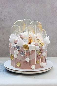 Light brown and golden colored birhtday cake with macaroons, coins, meringue and lollipops