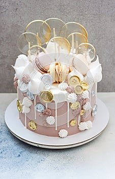 Light brown and golden colored birhtday cake with macaroons, coins, meringue and lollipops