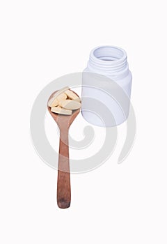 Light brown pills in pill on spoon wooden color brown with bottle white put on the side