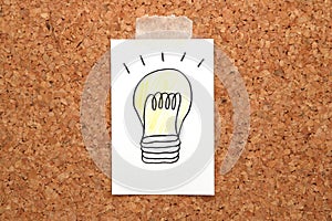 Light bulb drawn on white paper on cork board.