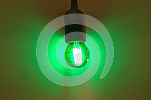 Light bulb glowing green on grey wall background