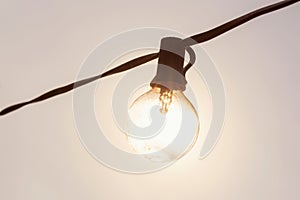 light bulb hanging on wire with sunshine background. energy concept