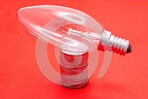 Light bulb on a pile of coins on red background. Saving electricity, money and economics connection