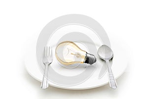 Light bulb in plate and fork and spoon isolated on white