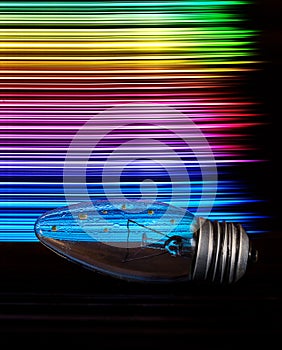 The light bulb is wet on the table and on the back are multi-colored stripes in the form of a rainbow. art photo