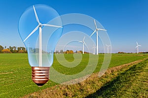 Light bulb with wind turbine inside on the background of blue sky and green field with turbines.