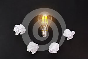 Light bulbs glows orange and crumpled paper on black background. Good idea and inspiration concept