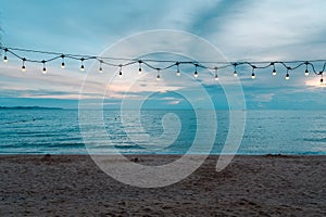 Light bulbs on string wire decoration at the party event festival on the beach at sunset. Outdoor holiday background. Copy space