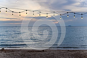 light bulbs on string wire decoration at the party event festival on the beach at sunset. Outdoor holiday background. Copy space