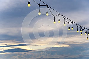 light bulbs on string wire decoration at the party event festival on the beach at sunset. Outdoor holiday background. Copy space