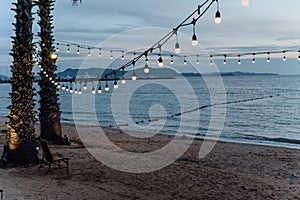 light bulbs on string wire decoration at the party event festival on the beach at sunset. Outdoor holiday background. Copy space