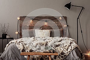 Light bulbs on wooden headboard of comfortable bed with grey bedding and warm fury blanket