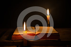 Light candle with holy bible and cross or crucifix on old wooden background in church.Candlelight and open book on vintage wood