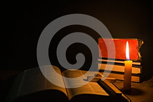 Light candle with holy bible and cross or crucifix on old wooden background in church.Candlelight and open book on vintage wood