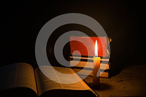 Light candle with holy bible and cross or crucifix on old wooden background in church.Candlelight and open book on vintage wood