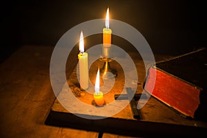 Light candle with holy bible and cross or crucifix on old wooden background in church.Candlelight and open book on vintage wood