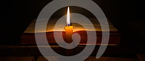 Light candle with holy bible and cross or crucifix on old wooden background in church.Candlelight and open book on vintage wood