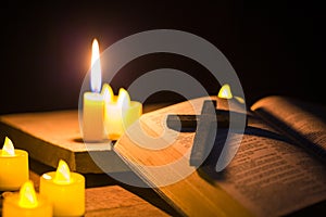 Light candle with holy bible and cross or crucifix on old wooden background in church.Candlelight and open book on vintage wood