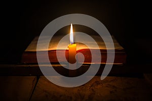 Light candle with holy bible and cross or crucifix on old wooden background in church.Candlelight and open book on vintage wood
