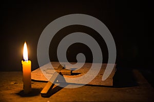 Light candle with holy bible and cross or crucifix on old wooden background in church.Candlelight and open book on vintage wood