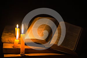 Light candle with holy bible and cross or crucifix on old wooden background in church.Candlelight and open book on vintage wood