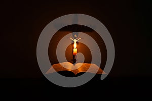 Light candle with holy bible and cross or crucifix on old wooden background in church.Candlelight and open book on vintage wood