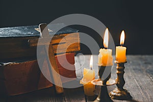 Light candle with holy bible and cross or crucifix on old wooden background in church.Candlelight and open book on vintage wood