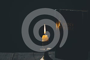 Light candle with holy bible and cross or crucifix on old wooden background in church.Candlelight and open book on vintage wood