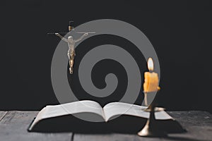 Light candle with holy bible and cross or crucifix on old wooden background in church.Candlelight and open book on vintage wood