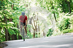 In light clothes. Cyclist on a bike is on the asphalt road in the forest at sunny day