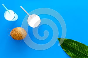 Light cocktail with coconut milk. White tropical beverage in glasses with straw on blue background with coconut and palm