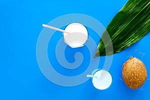 Light cocktail with coconut milk. White tropical beverage in glasses with straw on blue background with coconut and palm