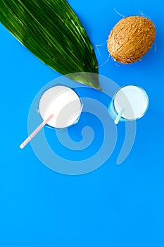 Light cocktail with coconut milk. White tropical beverage in glasses with straw on blue background with coconut and palm