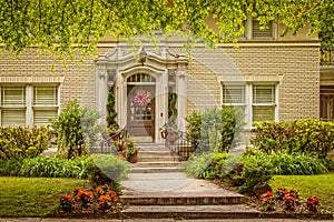 Light colored brick house with ornate entranceway and beautiful landscaping around sidewalk and steps leading up - framed by photo