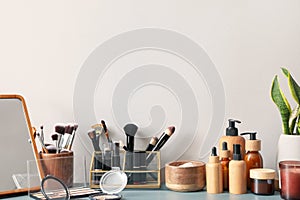 Different cosmetics with mirror and houseplant on table near light wall