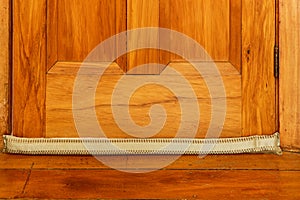 A light coloured draught stopper sits on the floor at the base of a wooden door