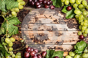 Light and dark grapes with leaves and vines on a wooden background, top view, frame