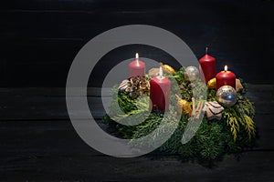 Light in the dark on third advent, natural green wreath with red candles, three are burning, Christmas decoration and cookies,
