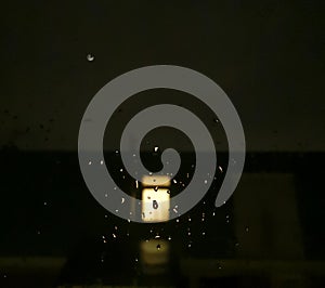 A light in the darkness at night with drops of rain on the window