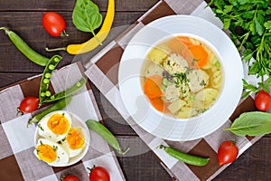 Light dietary soup with meat balls, vegetables, fusilli and boiled eggs on a dark wooden table.