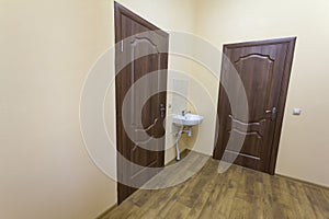 Light empty corridor hall with wooden floor, brown doors and sink. School, office or clinic interior