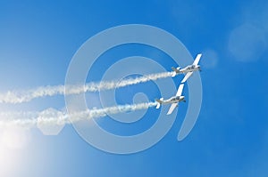 Light engine airplane with a trace of white smoke fly in groups in the blue sky with sunlight and glare.