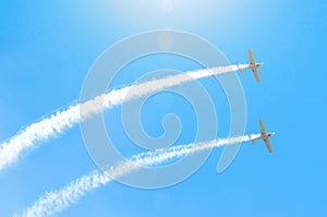 Light engine airplane with a trace of white smoke fly in groups in the blue sky with sunlight and glare.