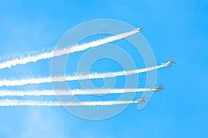 Light engine airplane with a trace of white smoke fly in groups in the blue sky with sunlight and glare.