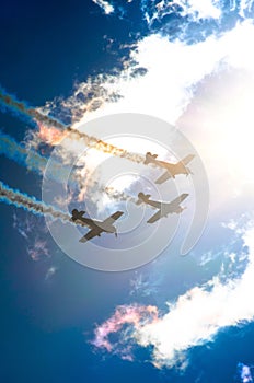 Light engine airplane with a trace of white smoke fly in groups in the blue sky with sunlight and glare.