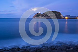 Light of Getaria lighthouse and fullmoon over the sea at night.