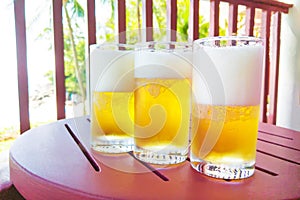 Light golden beer in glasses..Three steamed glasses with cold beer on a wooden table..Purple-red color table with drinks on the ba
