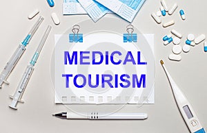 On a light gray background, blue medical masks, syringes, an electronic thermometer, pills, a pen and a notebook with the
