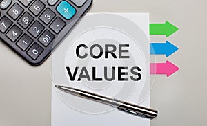 On a light gray background, a calculator, a white sheet with the text CORE VALUES, a pen and bright multicolored stickers. View