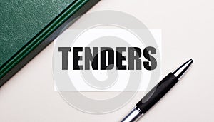 On a light gray background lies a pen, a green notebook and a white card with the text TENDERS. Business concept